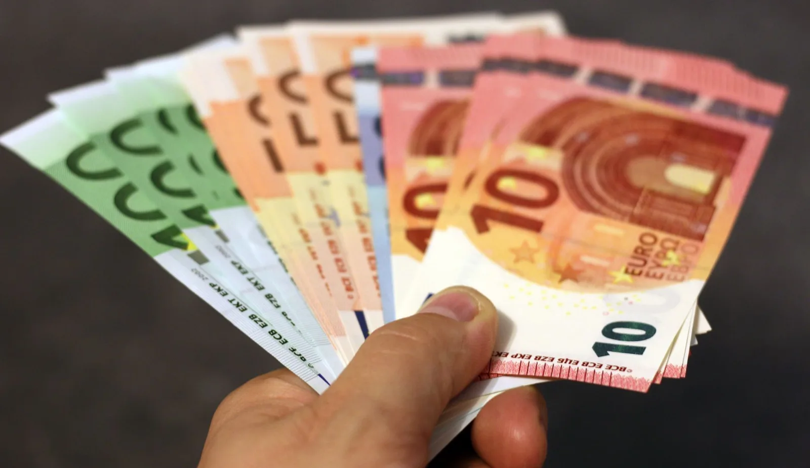 Un abanico de billetes de euro en varias denominaciones sostenido en una mano.